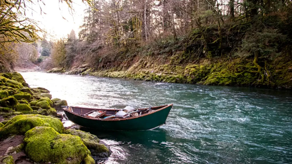 A drift boat tied off on a mossy bank of a clear green river, rigged for a guided float
