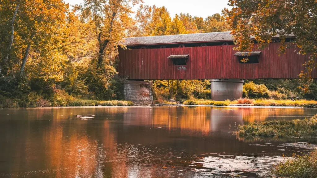 A red covered bridge crossing a river in full New England autumn