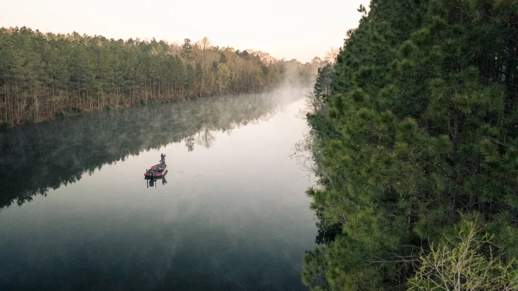 A small boat on flat water at first light against a wooded shore