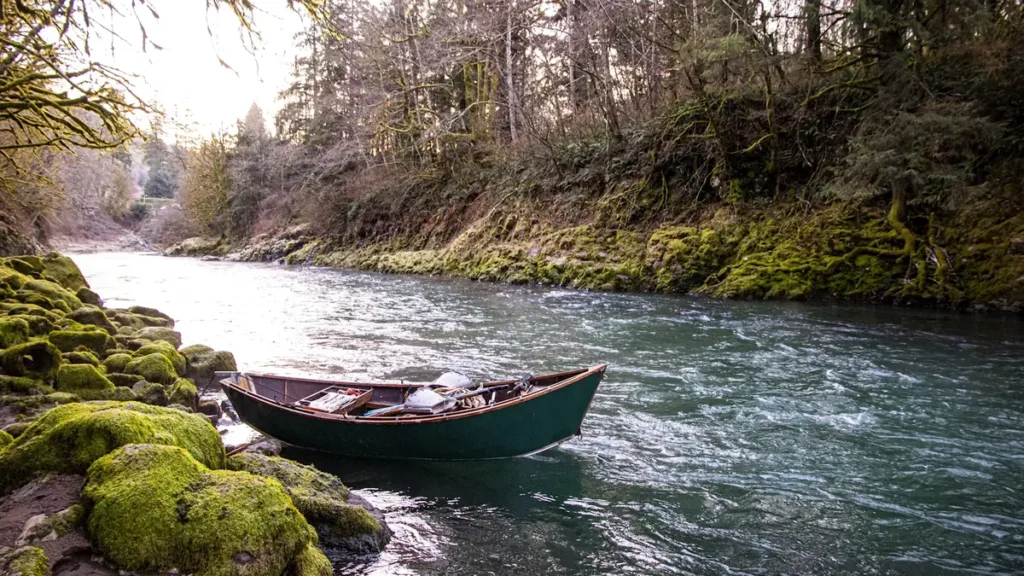 A wooden drift boat pulled onto a gravel bar on a Pacific Northwest river