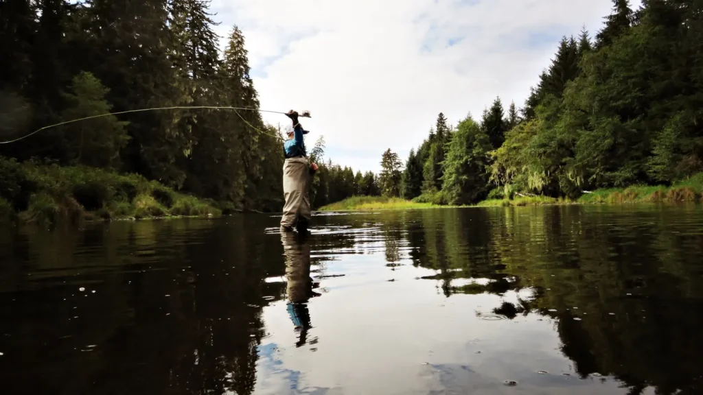 An angler swinging a two-handed rod on a forested Pacific Northwest river