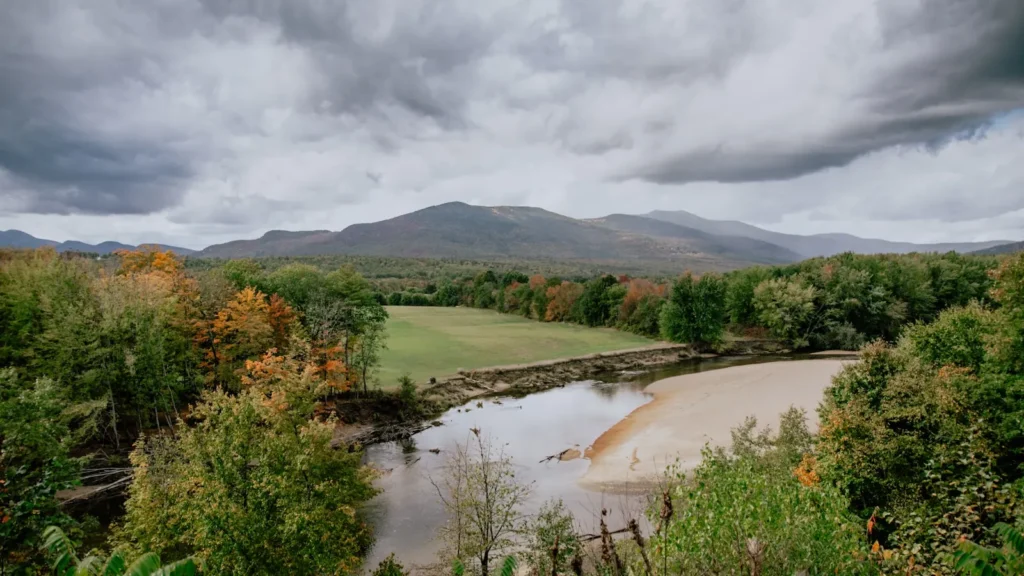 A broad river under fall colour with mountains beyond in New England