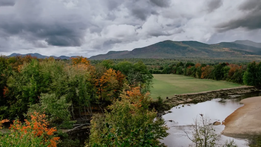 A New England river running past a sandbar below low mountains in autumn
