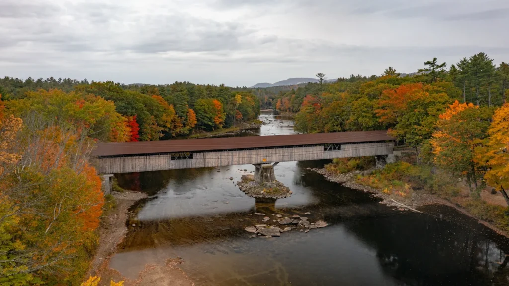 A bridge over a still river lined with autumn hardwoods in New England