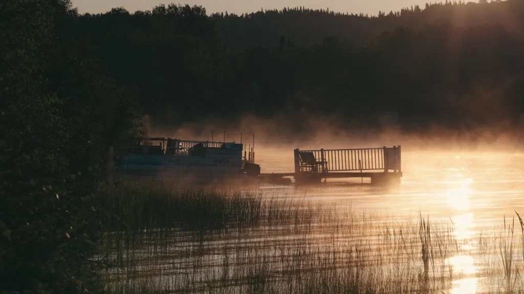 A dock and moored boat on a misty reservoir at sunrise