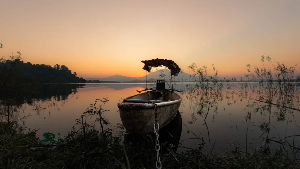 A small boat pulled up on a calm reservoir bank at sunset